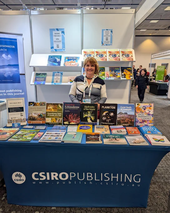 Elena Kupriyanova smiles, standing at the CSIRO Publishing conference booth behind a table full of books, including her book Hydroides of the World.