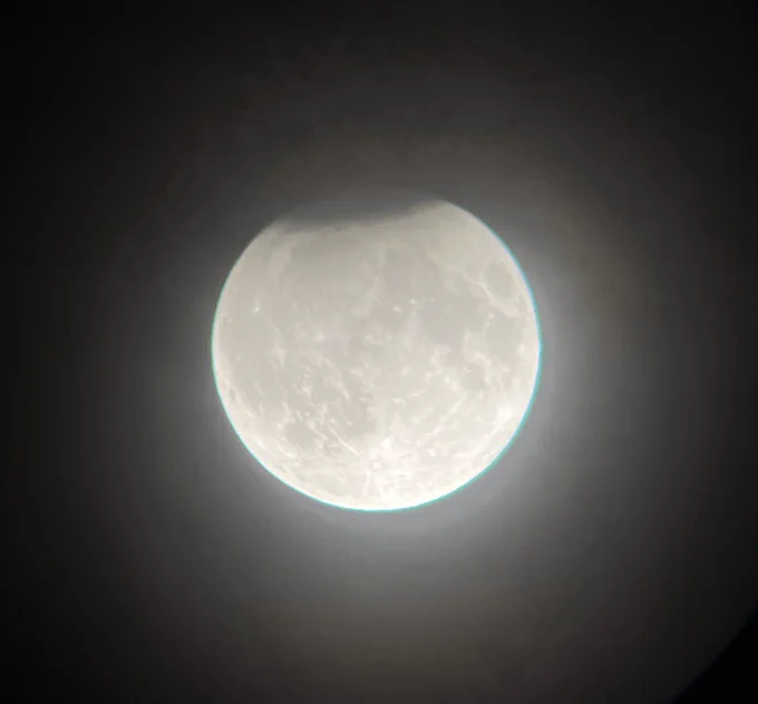 A poor photo of a partial lunar eclipse, with a small cap of dark on top of a full moon