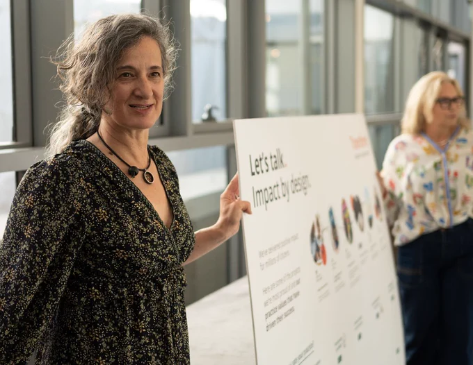 Person presenting a poster titled "Let's talk: Impact by design" at a conference.