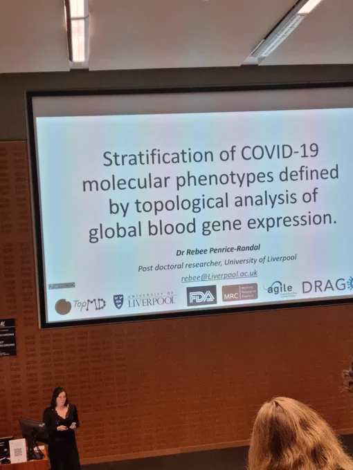 Rebee standing at the front of a lecture theatre, presenting her prior work on gene expression in COVID-19 patients
