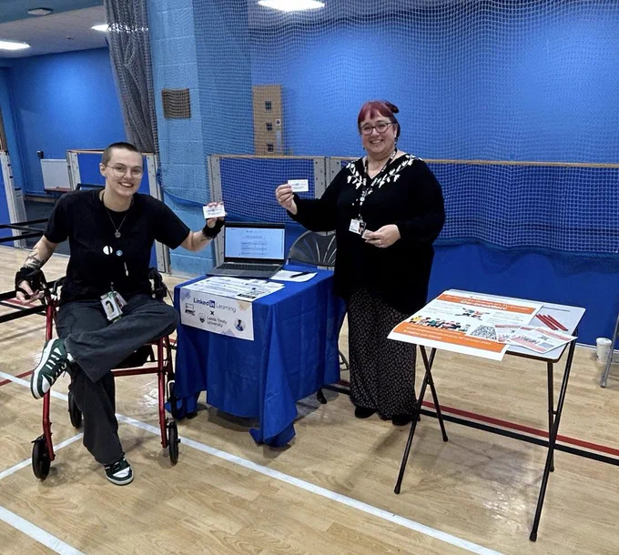 An image of a student and staff member holding LinkedIn Learning cards at the Leeds Trinity University Freshers’ Fair.