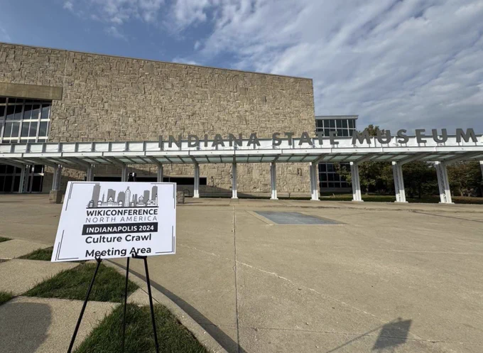 The front entrance of the Indiana State Museum. A sign in front says "WikiConference North America, Indianapolis 2024 Culture Crawl Meeting Area"