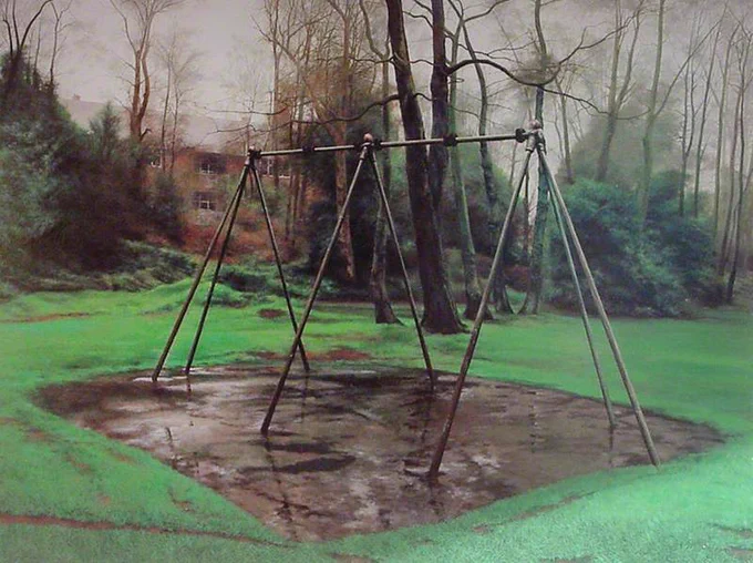A swing frame with no swings surrounded by grass and trees in the background on a grey day