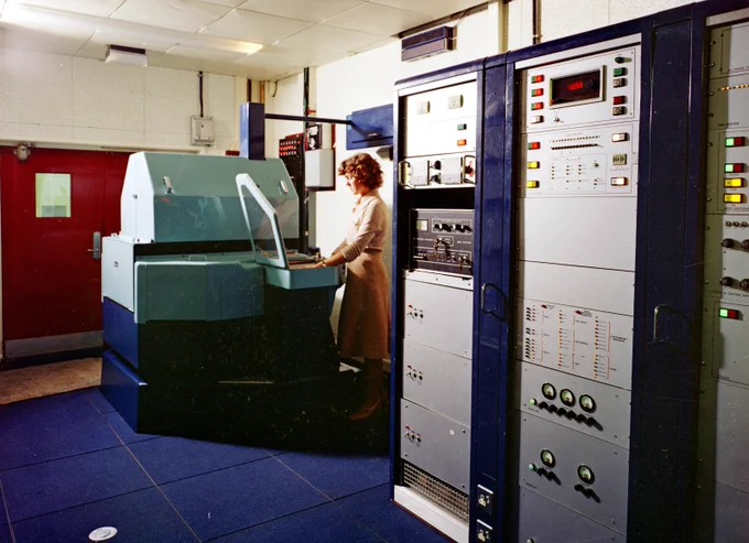 Woman standing with High Energy Physics laboratory. She is analysing bubble chamber film projected onto a surface.