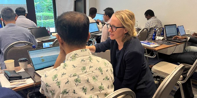 Attendees working on laptops at a business workshop, with one person pointing at another's screen, facilitating discussion.