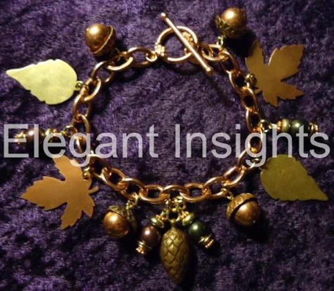 Our spectacular Scattered Leaves charm bracelet features leaves of various shapes and sizes along the length of a copper chain, secured with a toggle clasp. Between the brass and copper leaves are deep green and burgundy beads, as well as acorn and pinecone charms.