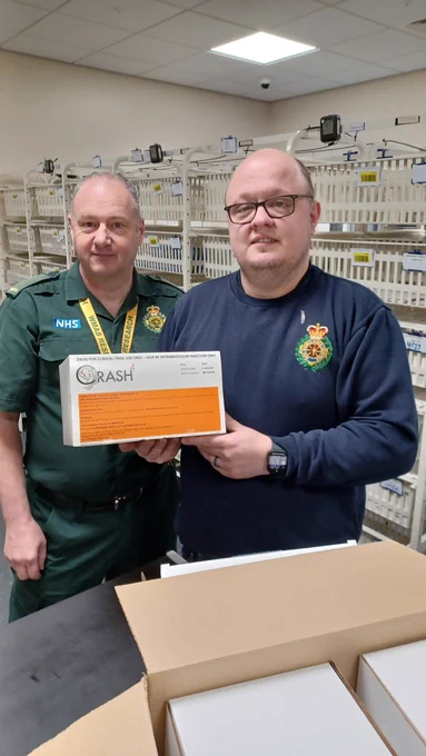 Paul and Matt stood in a medicines store room with a box of CRASH-4 medicines