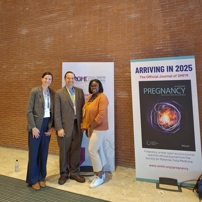 Taylor Bynarowicz, David Haas, and Jenifer Akinduro stand together in front of a poster. A poster next to them reads "Arriving in 2025, the Official Jorunal of SMFM" and contains a photo of the SMFM journal cover.