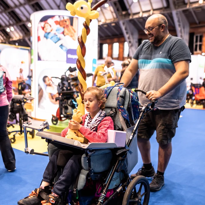 Picture captured from a previous Kidz to Adultz North event of a young child in a wheelchair being pushed by a male adult. 