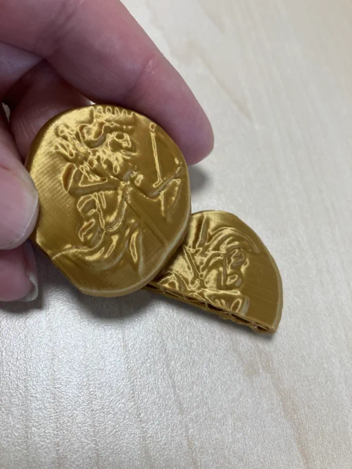 Picture of a 3D printed Daric being held in my hand, with a 3D printed coin cut in half beside it.