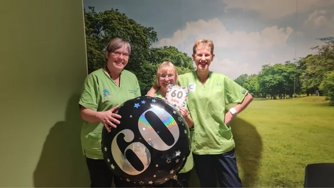 From left to right: Domestic Assistants Sharon, Donna and Louise. They are holding a balloon and a card with 60 on.