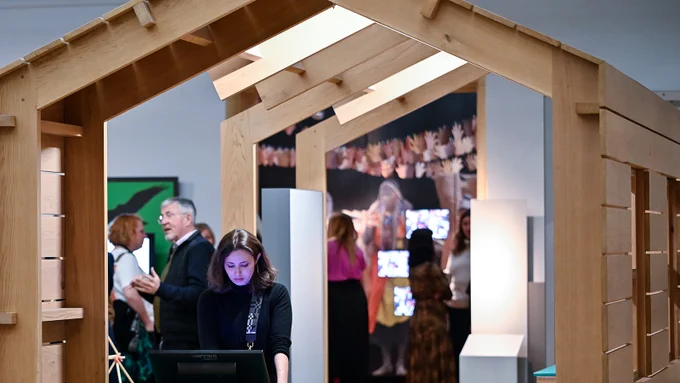 A person uses a screen interface in a museum space with large wooden beams overhead