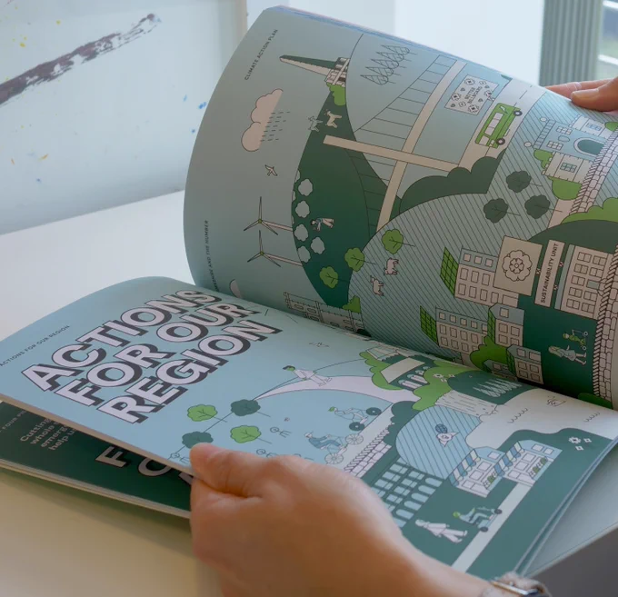 two hands hold an open report with a stylised representation of a Yorkshire and Humber landscape across the two pages. The heading reads 'Actions of our region'