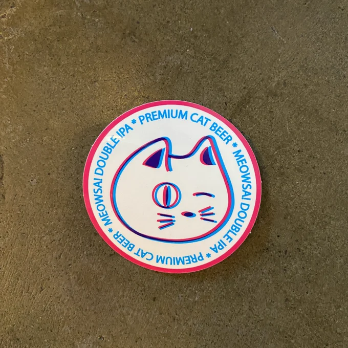 a round sticker with a cartoon cat that is printed in blue, then red and offset to look doubled with the words “premium cat beer meowsa double IPA” around the edge