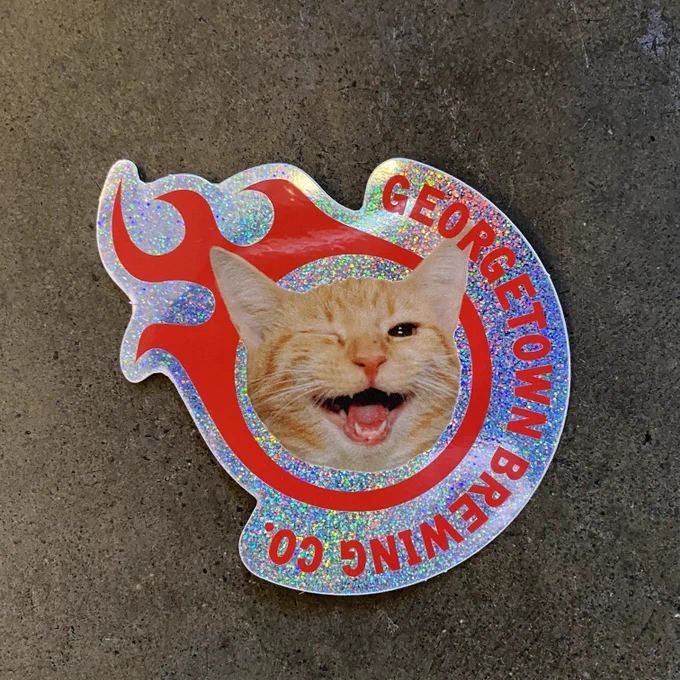 a glittery sticker with the georgetown gball and text that says georgetown brewing Company but has a winking orange cat instead of a big G