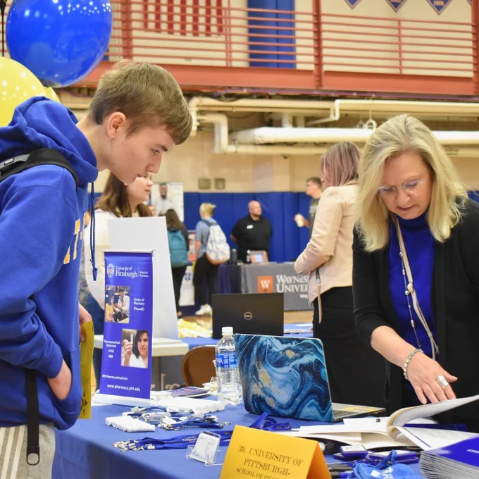 Graduate school representative speaking with student at information table.