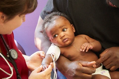A healthcare professional checking the blood pressure of a baby held by an adult.