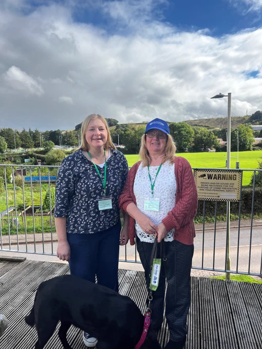 The image is Mandy from Devon in Sight, her guide dog Pepsi and Daniel from the Resilience Forum at the Crediton Rugby and Football club.  They are both smiling.