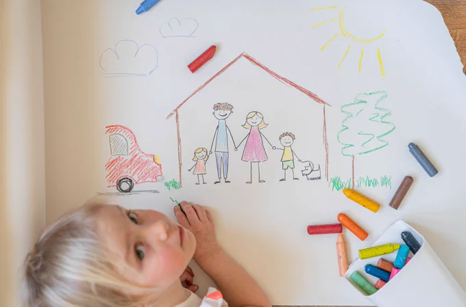 blonde hair child using crayons to draw house, with family and car