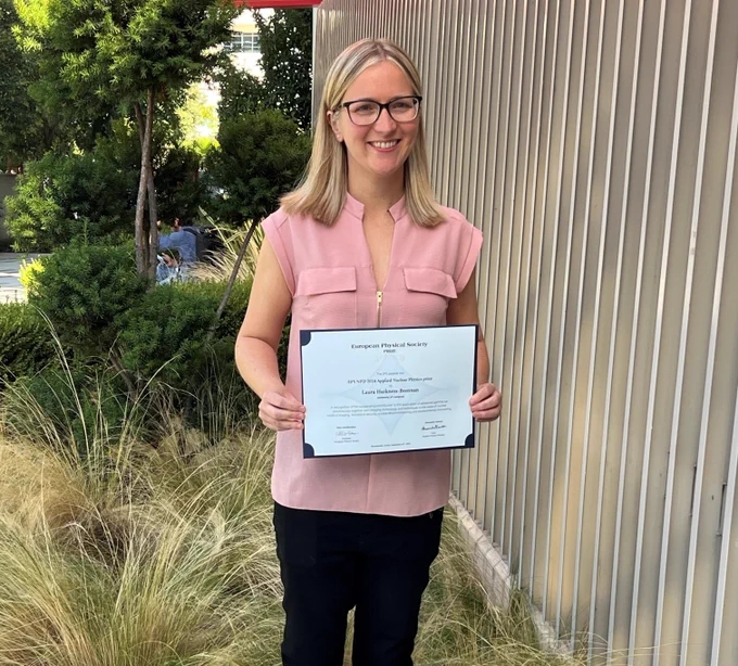 Laura stands proudly holding her prize with a background of trees and greenery.