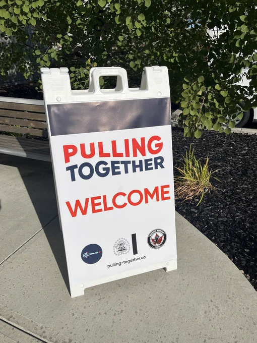 A folding sign on a sidewalk says, "Pulling Together - Welcome."