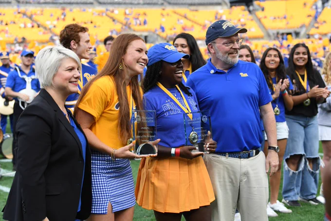 Two winners of the Spirit of Pitt award. Everyone is smiling and dressed in University of Pittsburgh colors.
