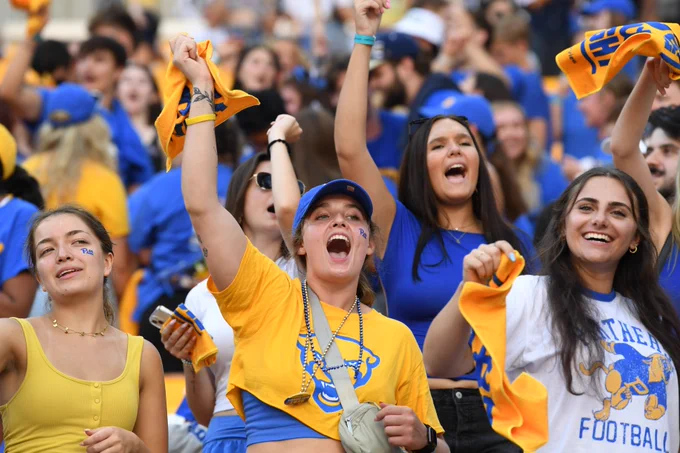 Enthusiastic fans in yellow and blue attire cheering at a Pitt football game.
