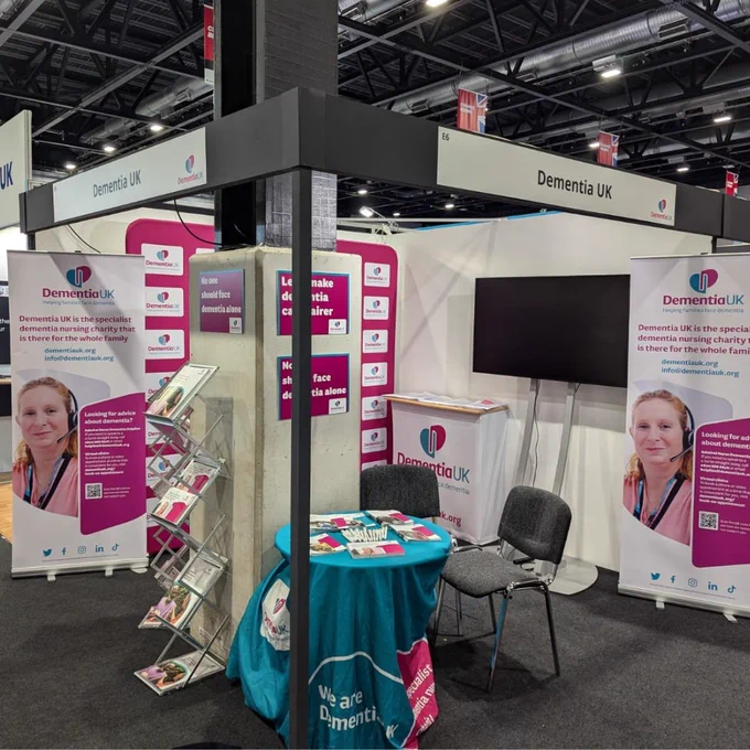 Booth of Dementia UK at the Labour Party conference featuring promotional banners, informational brochures, and various merchandise.