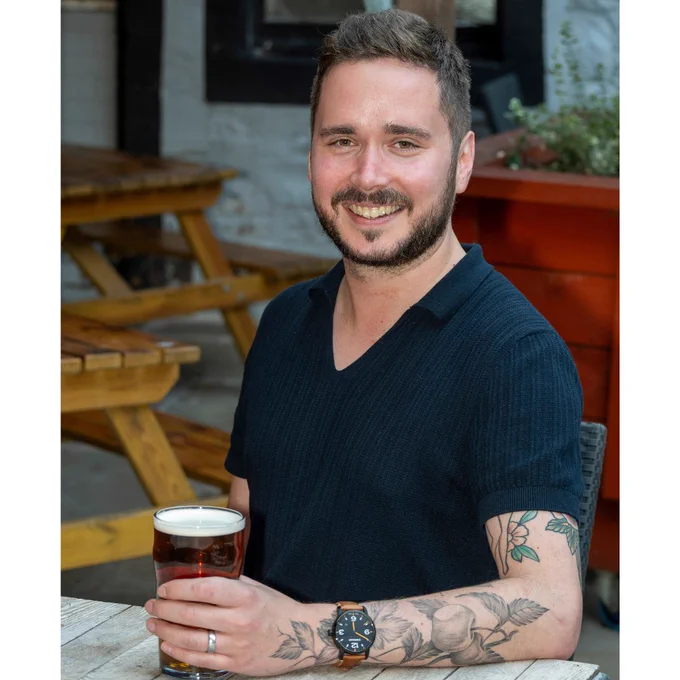 Photo of Ash Corbett-Collins in a pub beer garden holding a pint of beer.