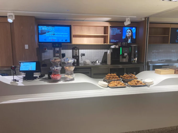 The cafe servery at the Pumphandle Social’s canteen. Muffins and other pastries can be seen, along with TV displays.