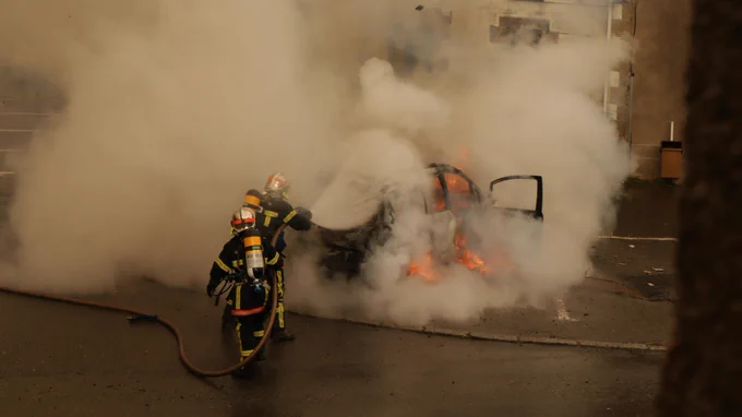 Two firefighters that are trying to extinguish a burning car. A lot of flames and smoke. Photo by Gwendal Bar on Unsplash