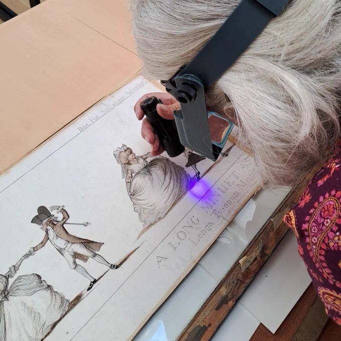 A person with an ultra violet light and magnifying glasses taking a close look at the Long Minuet print.