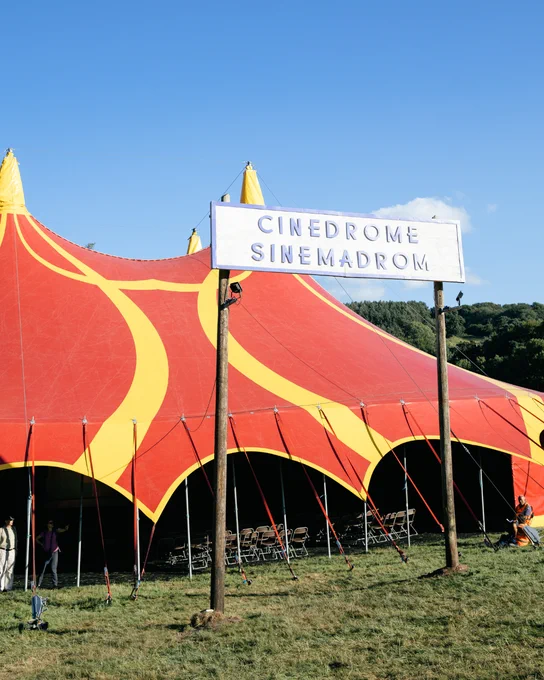 The Cinedrome, a large red and yellow circus tent, stands tall beneath clear blue skies at Green Man 2024.