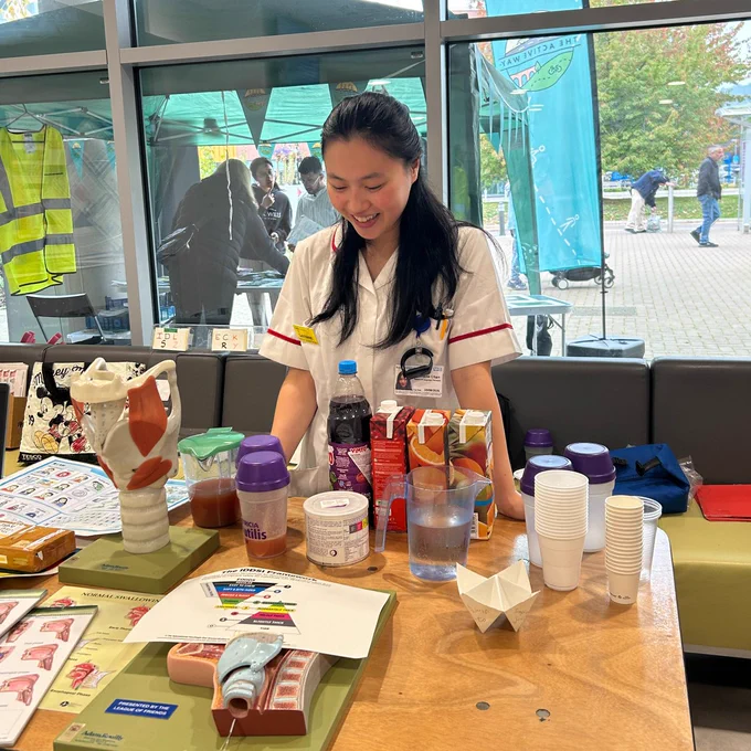 A member of therapies staff stands at a stall with a selection of drinks and anatomical models