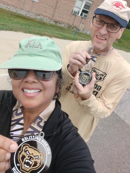 Sue Sil and Tom Fishwild holding participation medals to the 2024 Grizzly 10k run.