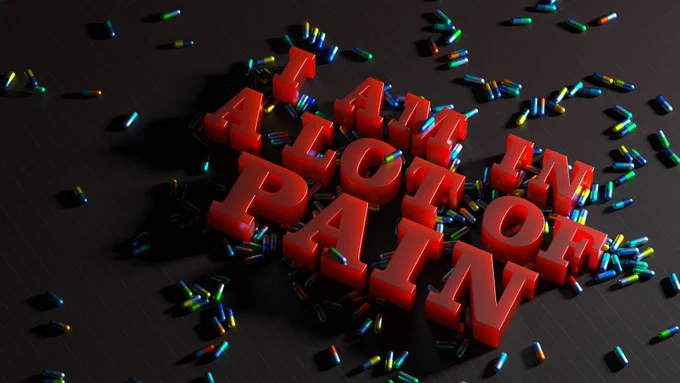 Red block letters say 'I am in a lot of pain' on a black background, medical pills are scattered about