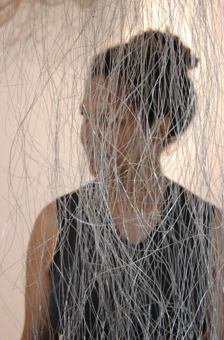 Maker Charmaine Lurch looking off to the side through the cascading metal wires of one of her works.