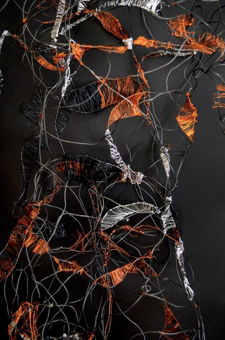 A detail of The Sycorax, a wire sculpture of the female form with the wire woven together with bright copper wire and black and white wires woven in dense sections to give weight to the body, as well as resembling leaves against a dark background.