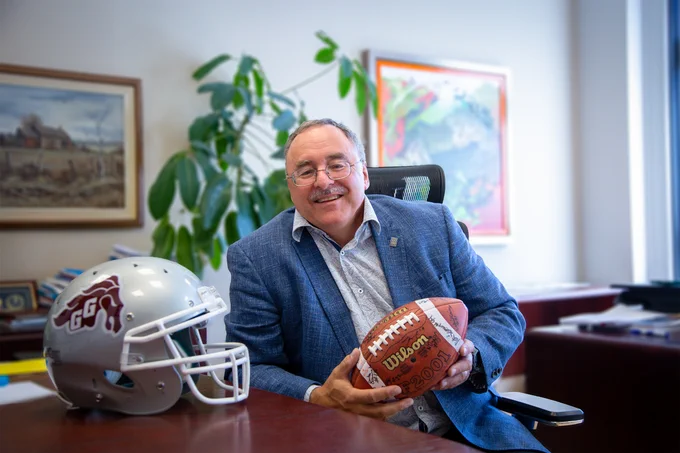 Sylvain Charbonneau takes a photo in his office with a Gee-Gees soccer helmet and a signed football. 