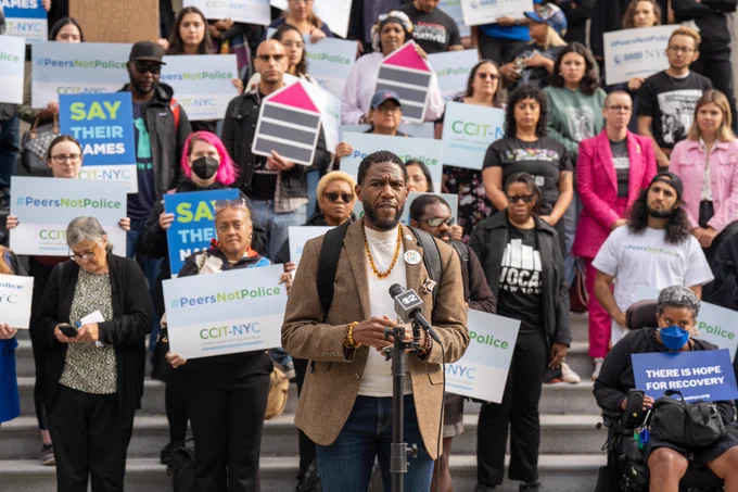 The Pubic Advocate speaks on the steps of City Hall, with advocates holding signs with. messages like "#PeersNotPolice" and "Say their names"