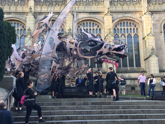 The Hatchling - A large dragon puppet stood at the top of the steps of Wakefield Cathedral. There are puppeteers holding her.