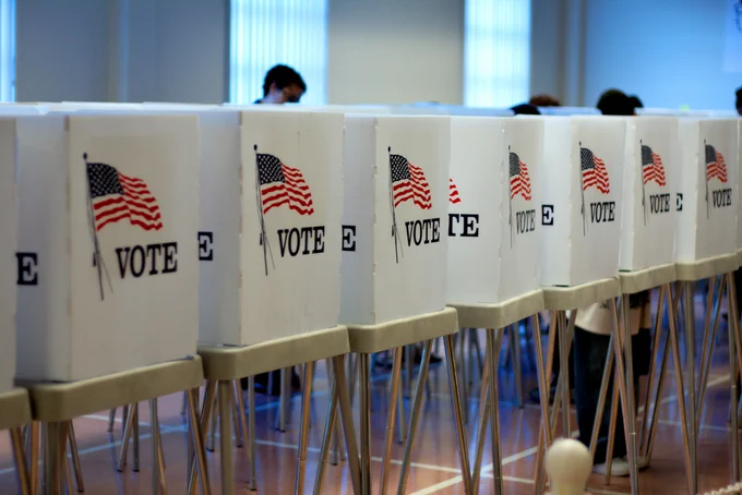 A row of voting booths with privacy covers that have an American Flag and read "Vote."
