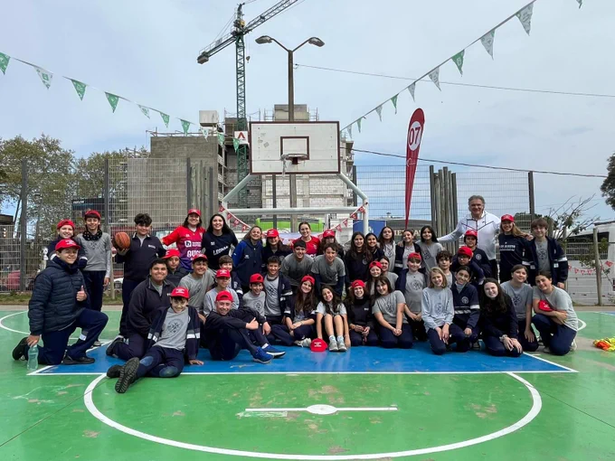 Grupo numeroso de adolescentes y jóvenes posan debajo del arco de una cancha de basquetbol. 