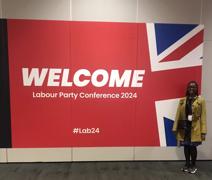 Black woman stands to the right of an image reading “Welcome Labour Party Conference 2024 hashtag Lab24