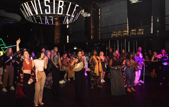 A crowd of people standing on a dancefloor facing the stage.