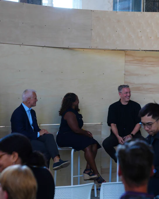 Three panelists seated on stools at a public speaking event.