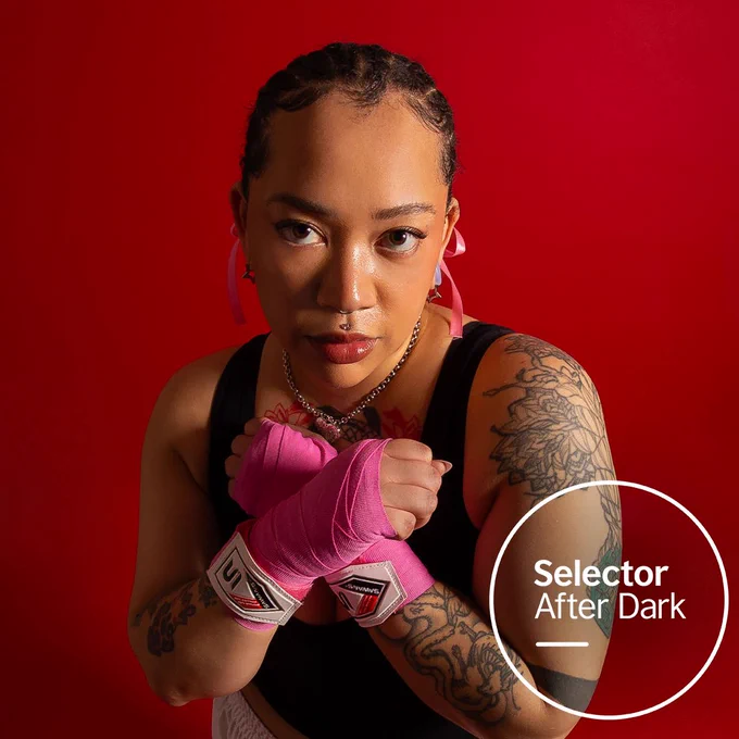 Press shot of iamkyami wearing boxing gear on a red background. On top of the image is the circular Selector After Dark logo in the bottom right hand corner.