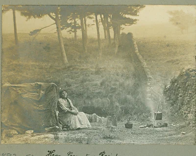 'Her country residence' by Sam Thompson, 1893. A sepia photograph of a woman sat in the countryside beside a tent and a fire. Lancashire Archives and Local History collections.