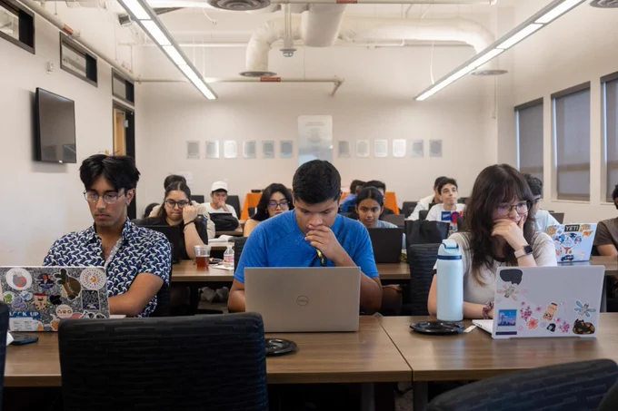 A black and white photo of multiple students in a classroom setting with laptops. In the row closest to the camera there are three students. They seem to appear to be focused on their screens with their hands held up to their mouths. Students in the rows behind them are doing the same thing. Courtesy of Seojin Yoon.