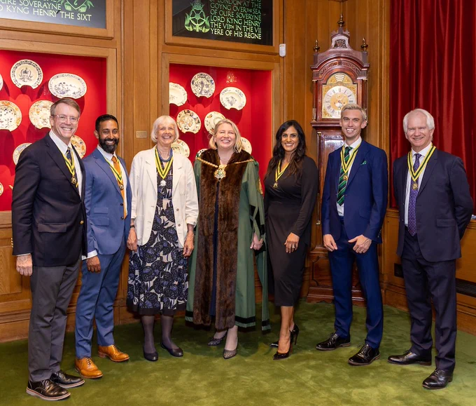 From L to R: Reade Fahs, Vijay Tailor-Hamblin, Sue Kevan, Liz Shilling wearing Master Spectacle Maker's gown and chain, Vinni Virdee, Greg Richardson and Christopher Bentley. All are smiling and dressed smartly. 